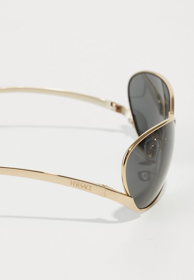 Versace solbriller med en guldmetalramme, mørke toneinntrengende linser og et strømlinet design. Har indgraveret branding på siden.