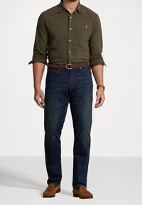 Oliwkowa koszula zapinana na guziki z podwiniętymi rękawami, niebieskie dżinsy, brązowy skórzany pasek i brązowe zamszowe mokasyny. Codzienny strój.