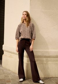 Leopárdmintás pulóver rövid ujjal, bordázott nyakkivágással, magas derekú barna trapéznadrággal és kényelmes fehér tornacipővel párosítva.