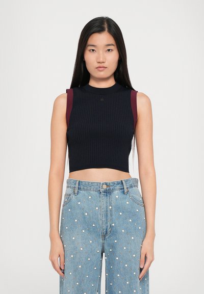 Crop top nero a coste con accenti amaranto sulle spalle e collo alto. Abbinato a jeans azzurri chiari con decorazioni a pois bianchi.