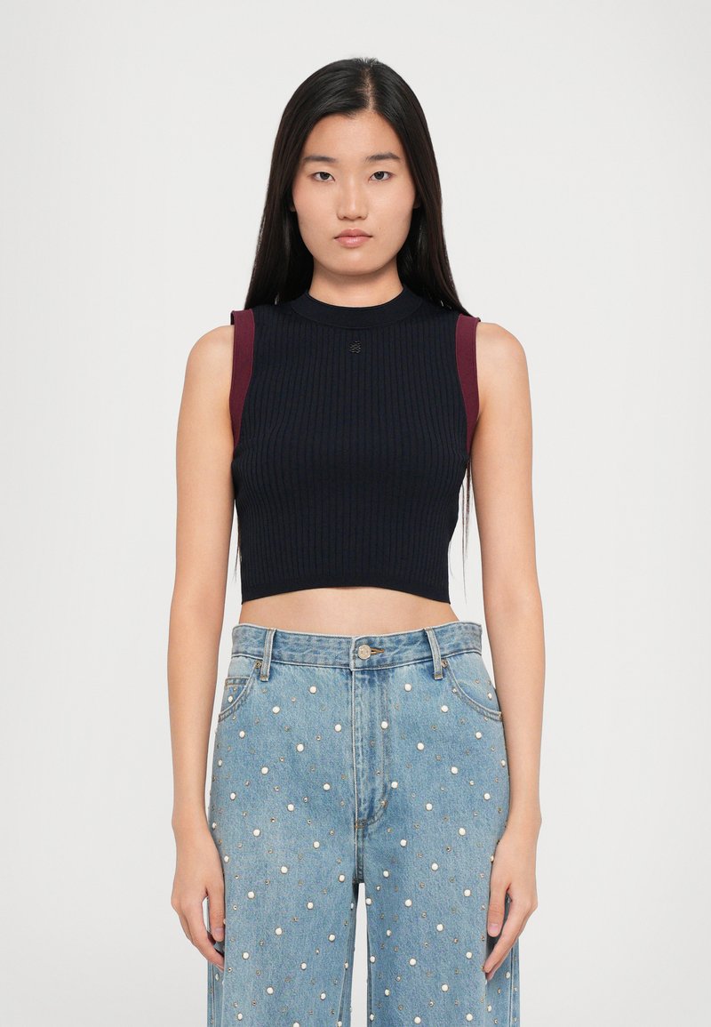 Čierny rebrovaný crop top s gaštanovými akcentmi na pleciach a vysokým golierom. Skombinovaný so svetlomodrými džínsy s ozdobami v podobe bielych bodiek.