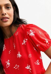 Rotes, strukturiertes Kleid mit weißen Blumenmustern, kurzen Puffärmeln und einem runden Ausschnitt, das subtile Details auf der Stoffoberfläche zeigt.