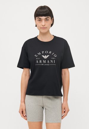 T-shirt in cotone nero con maniche corte, con logo e testo stampati in bianco. Abbinato a pantaloni corti a coste grigi. Look informale.