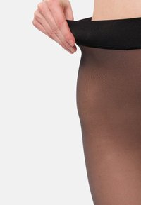 Pantys negros transparentes con una textura suave y translúcida. La cinturilla es gruesa y elástica, proporcionando un ajuste seguro.