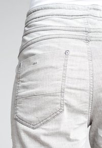 Gros plan sur un jean en denim gris clair montrant la poche arrière et la ceinture cousue sur un fond neutre.