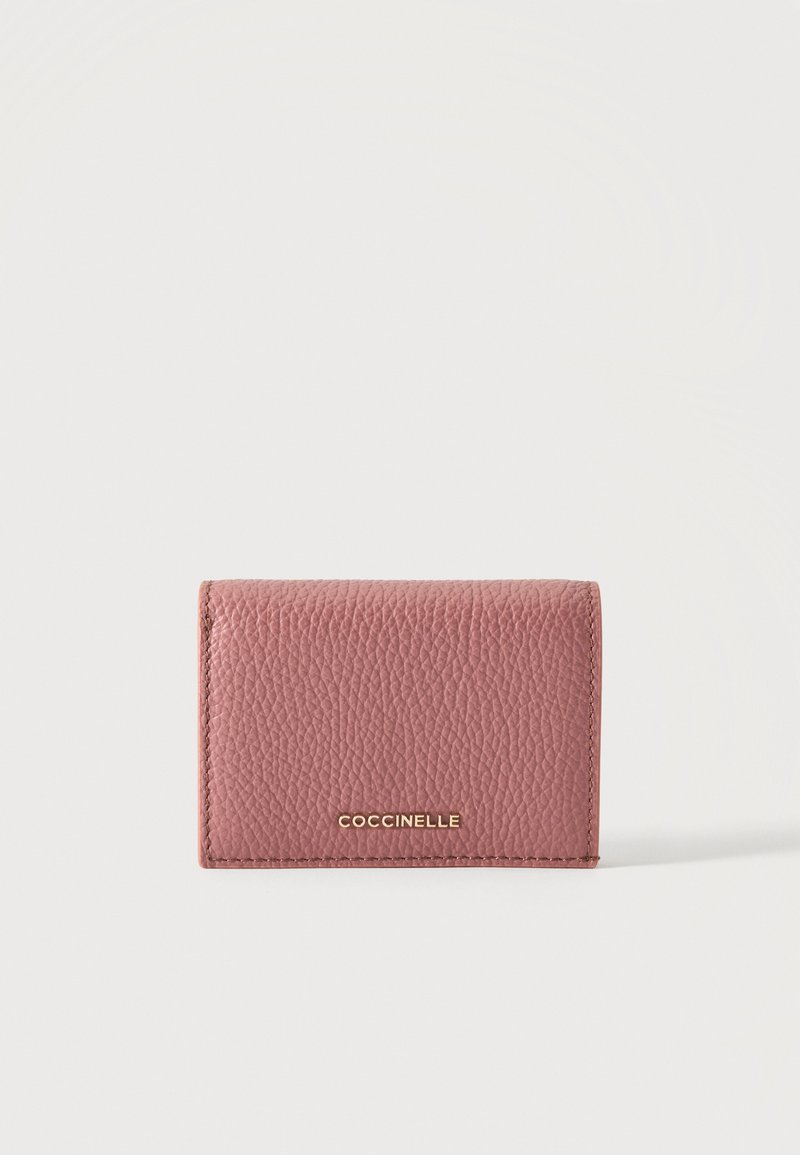 Portefeuille compact en cuir texturé rose avec logo doré "COCCINELLE" sur le devant, sur fond blanc uni.
