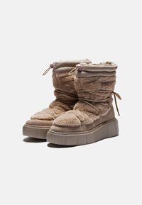 Bottes beiges en peluche, mi-mollet, avec un haut froncé, des lacets et une semelle épaisse et striée. Texture douce avec des accents lisses et une forme de bout arrondie.