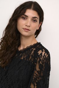 Black lace top with scalloped neckline and long sleeves. Sheer floral pattern with textured detailing. Soft drape and flowing fit.