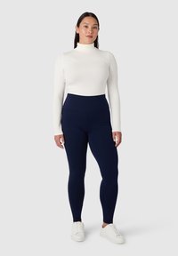 Maglietta bianca a manica lunga con collo alto abbinata a leggings blu navy a vita alta e sneaker bianche. Tessuto morbido e design aderente.