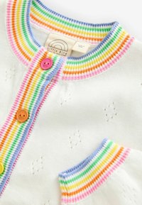 Cardigan bianco lavorato a maglia con un colletto a coste a righe multicolori e una fila di bottoni con bottoni rosa, arancioni e verdi.