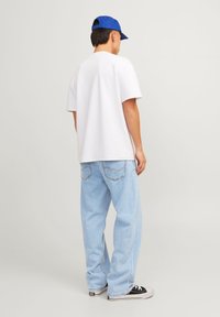 Vit bomull t-shirt med korta ärmar, ihopparad med ljusblå baggy jeans. Svarta sneakers med vit sula, blå keps som bärs bakåtvänd.
