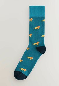 Teal sokker med ribbet manchet, prydet med et gentagende løvemønster i orange og gult. Mørk navy tå- og hælakkenter.