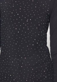 Haut à manches longues noir avec une texture lisse, décoré d'embellissements colorés en forme de gemmes disposés en motif de points.