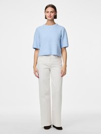 Světlomodrý žebrovaný svetr s krátkými rukávy a kulatým výstřihem, spárovaný s krémovými širokými kalhotami s vysokým pasem a tmavě hnědými botami.