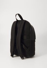 Svart ryggsäck med en texturerad nätbak, vadderade remmar och en stilren design. Utrustad med ett topphandtag och silverfärgade detaljer.