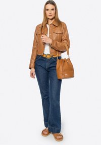 Giubbotto corto in pelle marrone, top bianco, jeans a zampa d'elefante blu, cintura marrone, borsa a secchiello marrone e sandali con piattaforma color sabbia e dettaglio a fibbia.