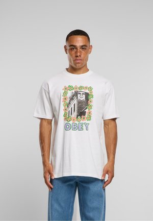 White cotton t-shirt featuring a graphic design with a flower border and the word "OBEY" in green, displayed on a figure.