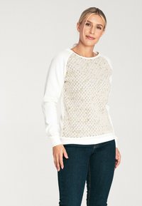 Bluza z długim rękawem o teksturowanym wzorze w owocach miodu w kolorze kremowym i jasnych pastelowych odcieniach, kontrastowe białe rękawy i dekolt, dopasowany krój.