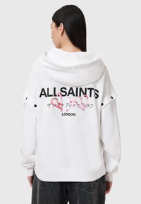 Sudadera blanca con un gran logotipo negro "ALLSAINTS" en la parte posterior, acentuado con corazones rosas y detalles en negro en los botones de las mangas.