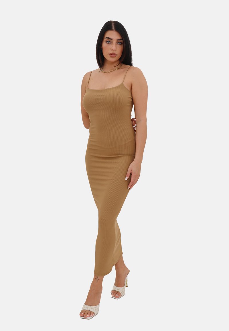 Abito midi a coste di colore beige con spalline sottili e una silhouette aderente, abbinato a sandali con tacco bianchi. Texture elegante, design minimal.