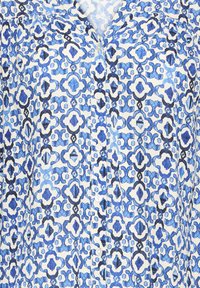 Blouse à motif géométrique bleu et blanc avec un devant à boutons et un col en forme de V.