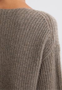 Zachte, bruine gebreide trui met ribbelstructuur, brede halslijn en verlaagde schouders, die een gezellige en warme uitstraling heeft.