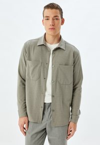 Grå långärmad skjorta med krage, två bröstfickor och knappstängning, kombinerad med ljusgrå randiga byxor.