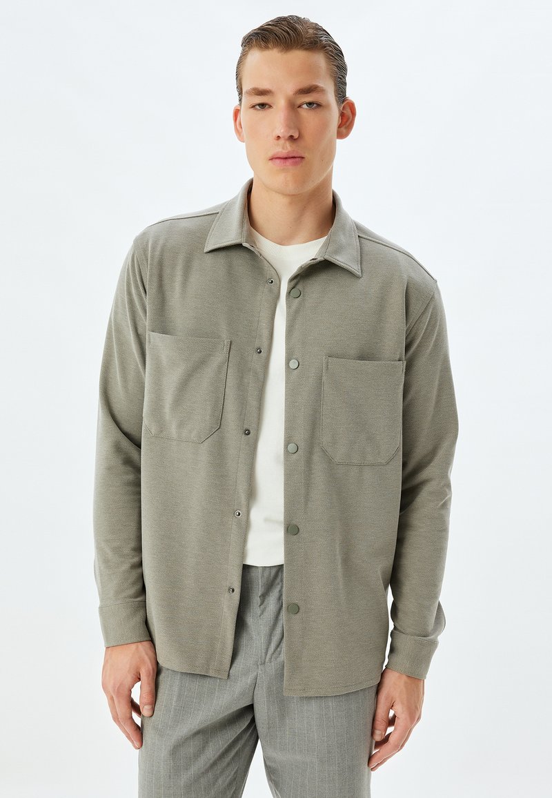 Grå långärmad skjorta med krage, två bröstfickor och knappstängning, kombinerad med ljusgrå randiga byxor.