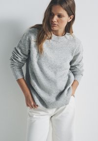 Maglione lavorato a maglia grigio chiaro con scollo e polsini a coste, caratterizzato da una vestibilità rilassata e una texture sottile, abbinato a pantaloni bianchi a gamba larga.
