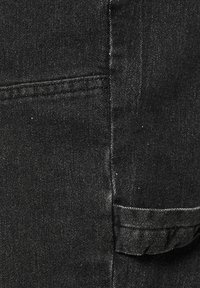 Nahaufnahme von schwarzem Denimstoff mit detaillierter Naht und einer kleinen umgeschlagenen Taschenklappe.