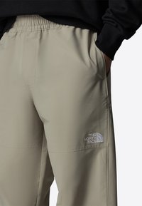 Beiga soft-shell byxor med elastisk midja, sidofickor och broderad logotyp på nedre vänstra benet. Slät textur och strömlinjeformad design.