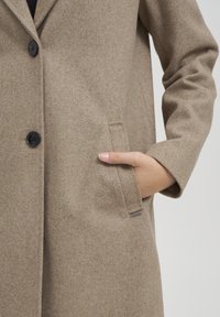Cappotto in misto lana marrone chiaro con bottoni neri, design monopetto e tasca laterale. Tessuto testurizzato, forma classica e sartoriale.