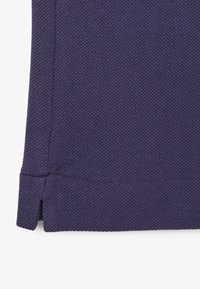 Mörk lila tyg med en strukturerad mönster, som visar fållkanten med små sidoklipp för extra detalj.