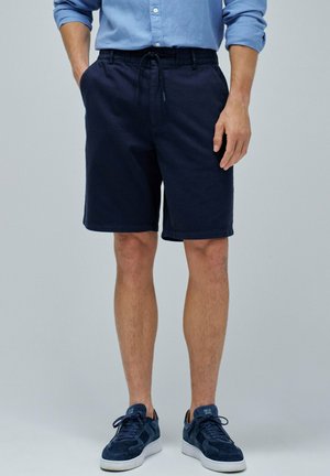 Shorts en coton bleu marine pour homme avec une taille élastique et un cordon de serrage, dotés de deux poches latérales et d'une coupe décontractée. Associés à des baskets bleu marine.