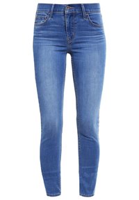 Jeans skinny de denim azul con diseño de cinco bolsillos, cierre de botón y costuras cosidas. La tela presenta una textura suave y ligeramente desgastada.