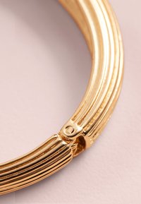 Armreif in Goldoptik mit strukturiertem Design, glatter Oberfläche und sicherem Verschlussdetail. Die Oberfläche ist reflektierend und poliert.