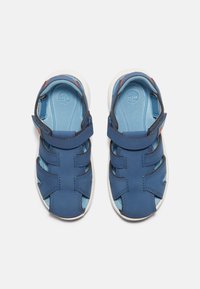 Siniset nahkasandaalit valkoisella pohjalla, joissa on useita hihnoja ja tarrakiinnitys. Vaaleansininen sisäpohja, jossa on logotieto.