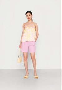 Top de alças floral amarelo claro e rosa, calções rosa, sandálias amarelas e uma pequena mala amarela. Tecido suave e design casual.