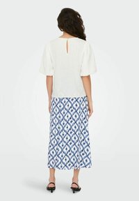 Blouse blanche texturée à manches bouffantes, associée à une jupe longue jusqu'au sol à motifs bleus et blancs, avec un détail dos en forme de goutte.