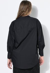 Camicia nera oversized con bottoni, maniche lunghe, realizzata in cotone morbido, con colletto classico e orlo arrotondato.