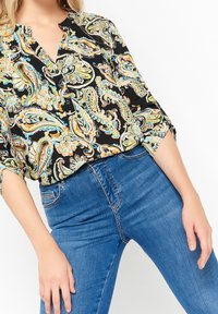 Svart blus med färgglad paisleymönster, V-ringning, knapplist och uppvikta ärmar. I kombination med blå jeans för en avslappnad look.