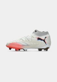 Biele a červené kopačky s vysokými ponožkami, textúrovaný povrch, šnúrky a čierne logo Puma na boku na jednoduchom pozadí.