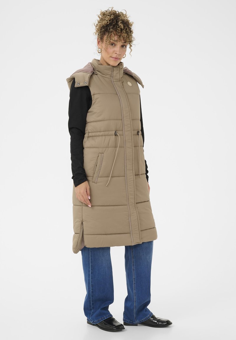Beige puffer-anku, jossa on korkea kaulus, sivutaskut ja säädettävä nyöri. Yhdistetty sinisten leveälahkeisten farkkujen ja mustien kiiltävien kenkien kanssa.