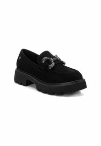 Mocasines de ante negros con suelas de goma gruesa, que presentan una hebilla metálica decorativa. Textura suave con diseño de punta redonda.