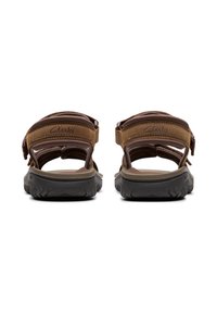 Sandalias de cuero marrón con correas ajustables, plantilla acolchada y suela exterior de goma negra texturizada, con la marca "Clarks" estampada.