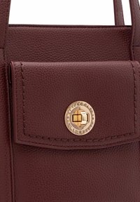 Burgunderfarbene Lederhandtasche mit strukturiertem Finish, einer Fronttasche mit goldfarbener, runder Druckknopfverschluss und sichtbaren Nähten.