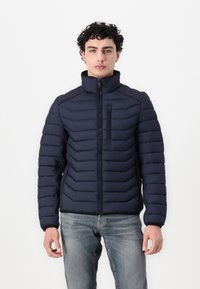 Jachetă puffer navy cu guler înalt, dotată cu un buzunar pe piept cu fermoar, design cu quiltat orizontal și manșete elasticizate.