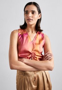 Satin ermeløs topp i gradient rosa og oransje med V-hals og snorjustering i midjen. Glatt tekstur, lett stoff.