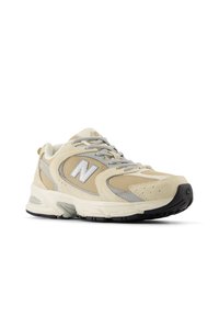 Sapatos de corrida bege e cinza com um superior em malha, painéis texturizados e uma sola de boracha escura. Apresenta o logo 'N' em relevo de um lado.