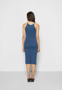 Vestido midi azul, ajustado ao corpo, com alças finas, costas recortadas e uma pequena fenda na barra. Feito de um tecido liso e elástico.